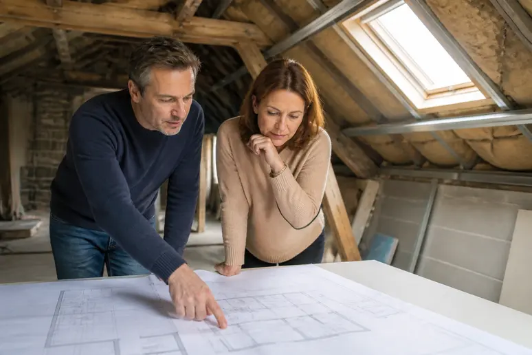 Couple français discutant des plans d'aménagement de leurs combles, avec un focus sur la planification des travaux.