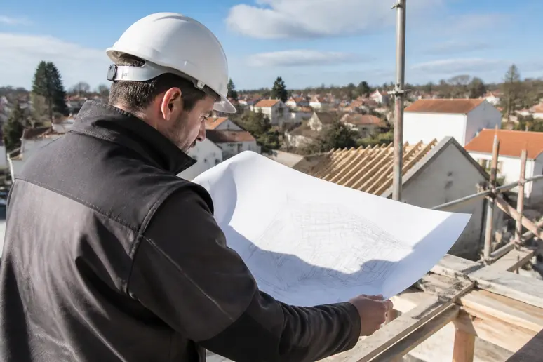Un couvreur français analyse les plans pour la construction d'une extension de toit, soulignant la précision des travaux.