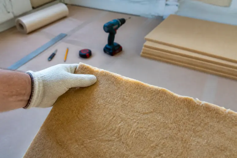 Gros plan sur un échantillon d'isolant en fibre de bois tenu par une main gantée, illustrant le choix des matériaux.