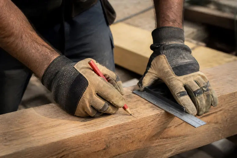 Les mains habiles d'un charpentier ajustent une pièce de bois, illustrant la précision dans la composition d'une charpente solide.
