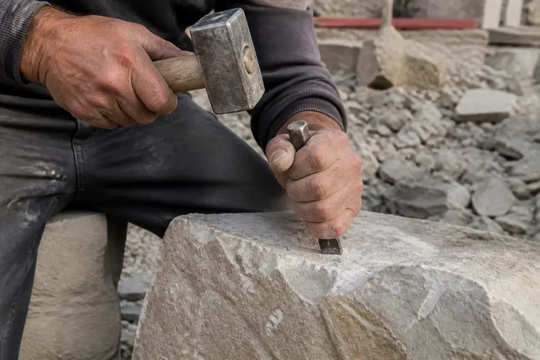 Les mains d'un tailleur de pierre français travaillent avec précision un bloc de calcaire local, soulignant l'artisanat traditionnel.