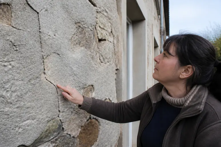 Propriétaire observant attentivement l'état de sa façade en pierre, détaillant les fissures.