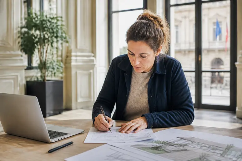 Femme française remplissant méticuleusement un formulaire de déclaration préalable pour des travaux d'aménagement extérieur.