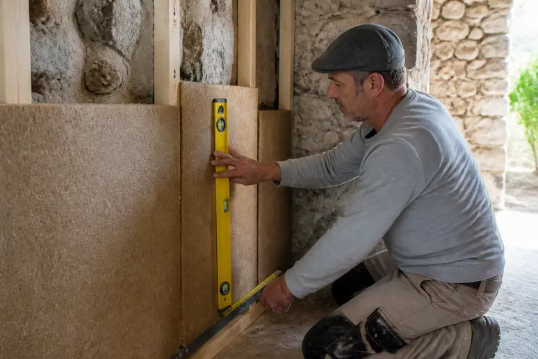Artisan français installant une isolation biosourcée dans une maison en pierre authentique.