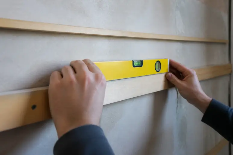Pose de tasseaux en bois sur un mur pour respecter les règles de ventilation du lambris.