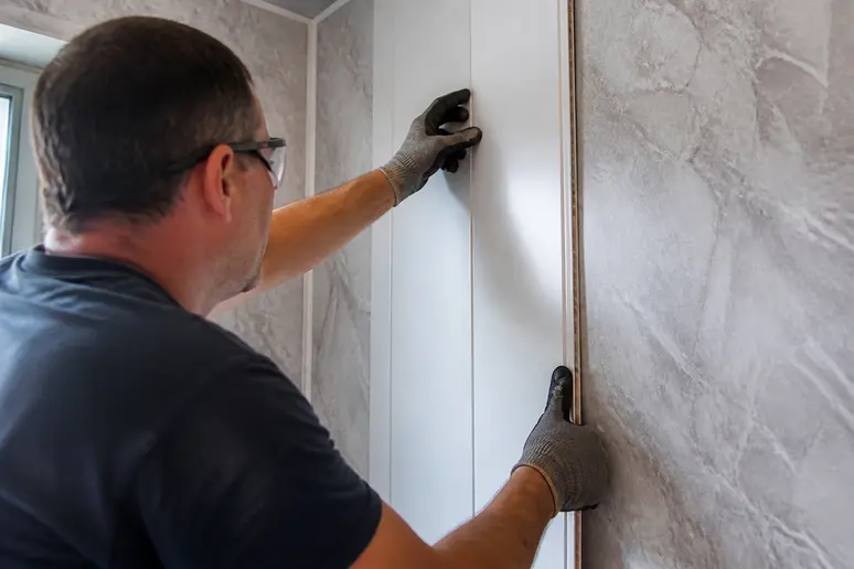 Installation de lambris en PVC étanche sur une cloison intérieure de salle d'eau.