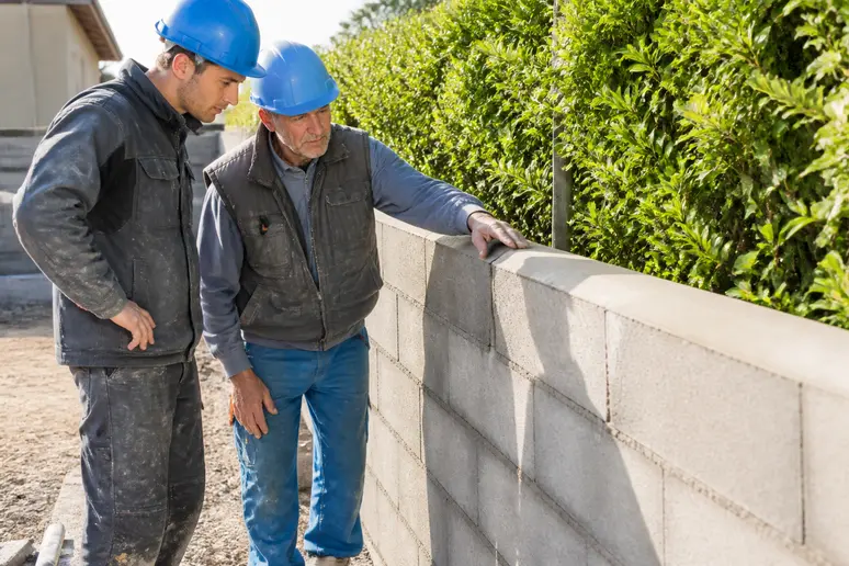 Des ouvriers français discutent et inspectent un mur de clôture en parpaings fraîchement construit.