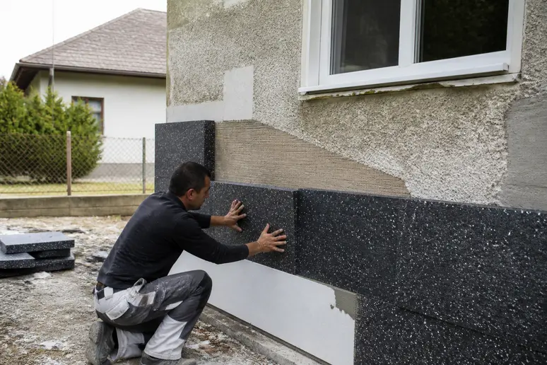 Artisan posant des panneaux d'isolation thermique sur la façade extérieure d'une maison ancienne