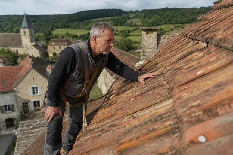 Un couvreur français inspecte méticuleusement la pente d'une toiture en tuiles romanes canal traditionnelles.